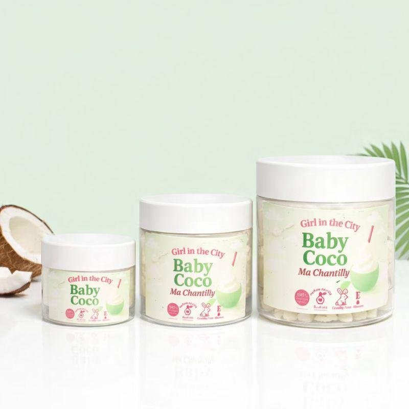 Beurre corporel fouetté coco light en pot transparent, texture aérienne de chantilly de karité, mise en scène avec éclats de coco et feuille de palmier.